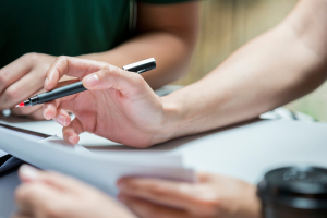 Up close image of hands holding documents. One person is holding a pen. This is to illustrate the main theme of North Carolina Trust Administration.