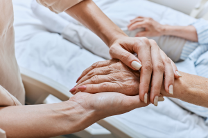 Image of a woman holding the hand of an older woman who is in a hospital bed to illustrate hospice care in Durham and Chapel Hill