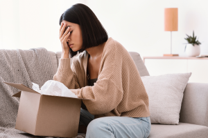 Photo of a woman covering her face. She has an empty box she's unpacking in front of her. This illustrates top probate mistakes in North Carolina.