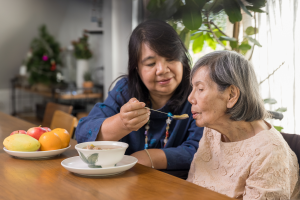 Image of an adult daughter feeding her elderly mother. This is to illustrate the question of guardianship vs trust for a loved one who is losing capacity.