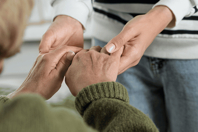 Image of a caregiver holding an elderly person's hands. This illustrates the idea of support for unpaid caregivers in North Carolina.